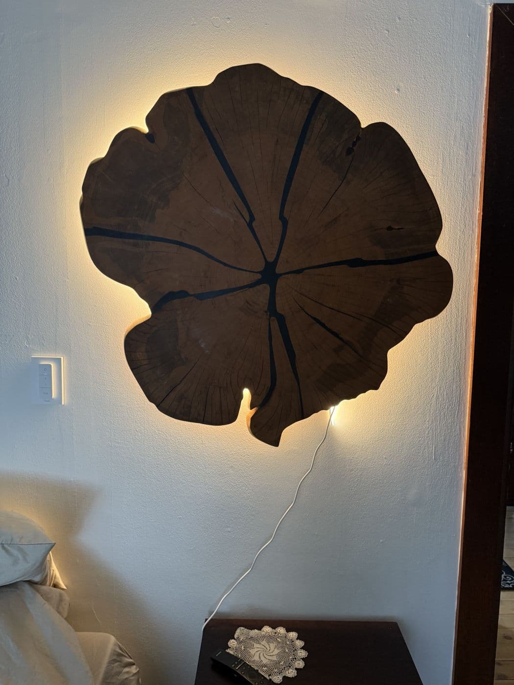 Backlit live-edge wood slab mounted on a bedroom wall, glowing warm around its edges